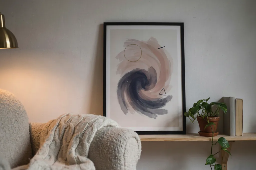 View from a seated position in a reading chair looking at one wall with a single large framed abstract celestial print at seated eye level, a trailing plant on a low shelf and warm lamp light