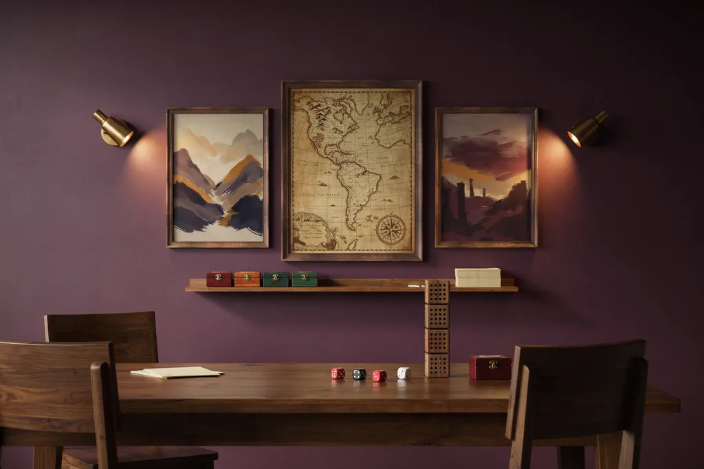 Gallery wall above a long wooden gaming table with a large framed fantasy map centered between two narrower art prints, and a slim shelf below holding dice boxes and a dice tower