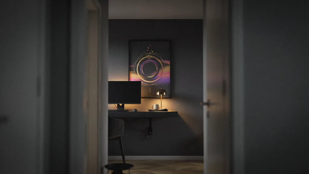 Small gaming room with a wall-mounted desk, warm bias lighting behind the monitor and one large framed art print above the desk