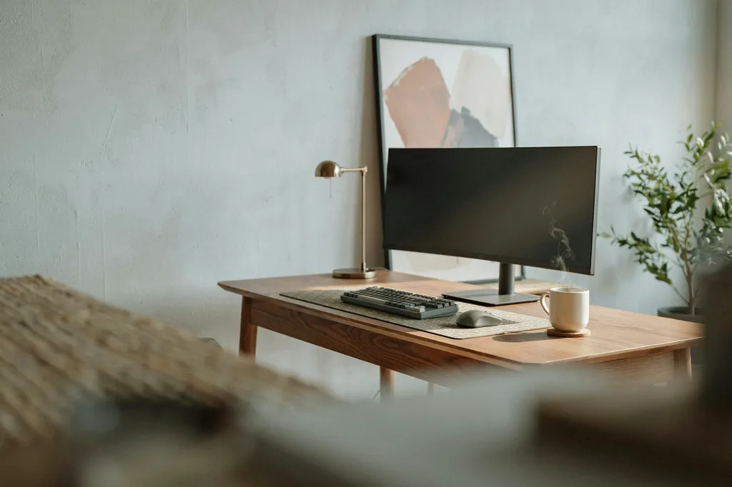 Minimal grown-up gaming desk in a bright living room with a walnut desk, patterned desk mat, one large framed print and a brass lamp