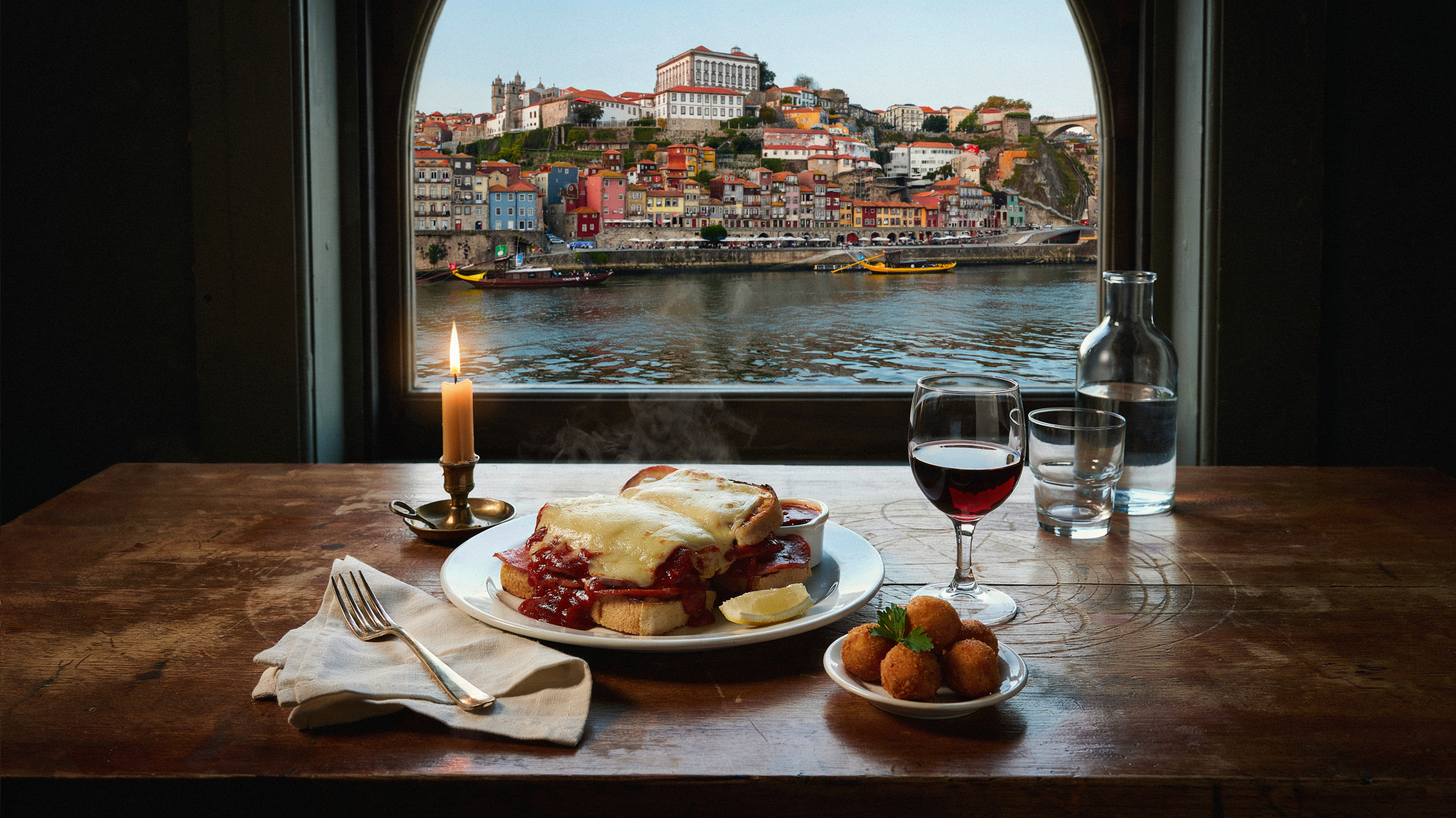 Porto riverside restaurant table with francesinha sandwich and glass of port wine overlooking the Douro River
